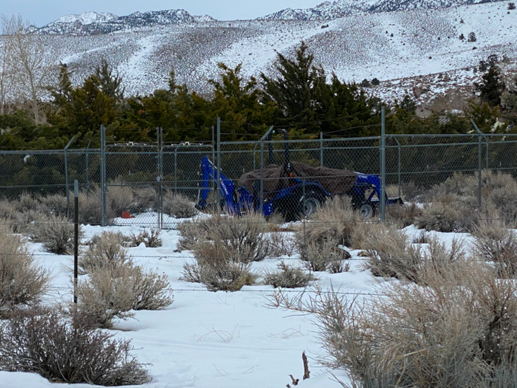 A blue tractor covered by a tarp in a fenced "cage."