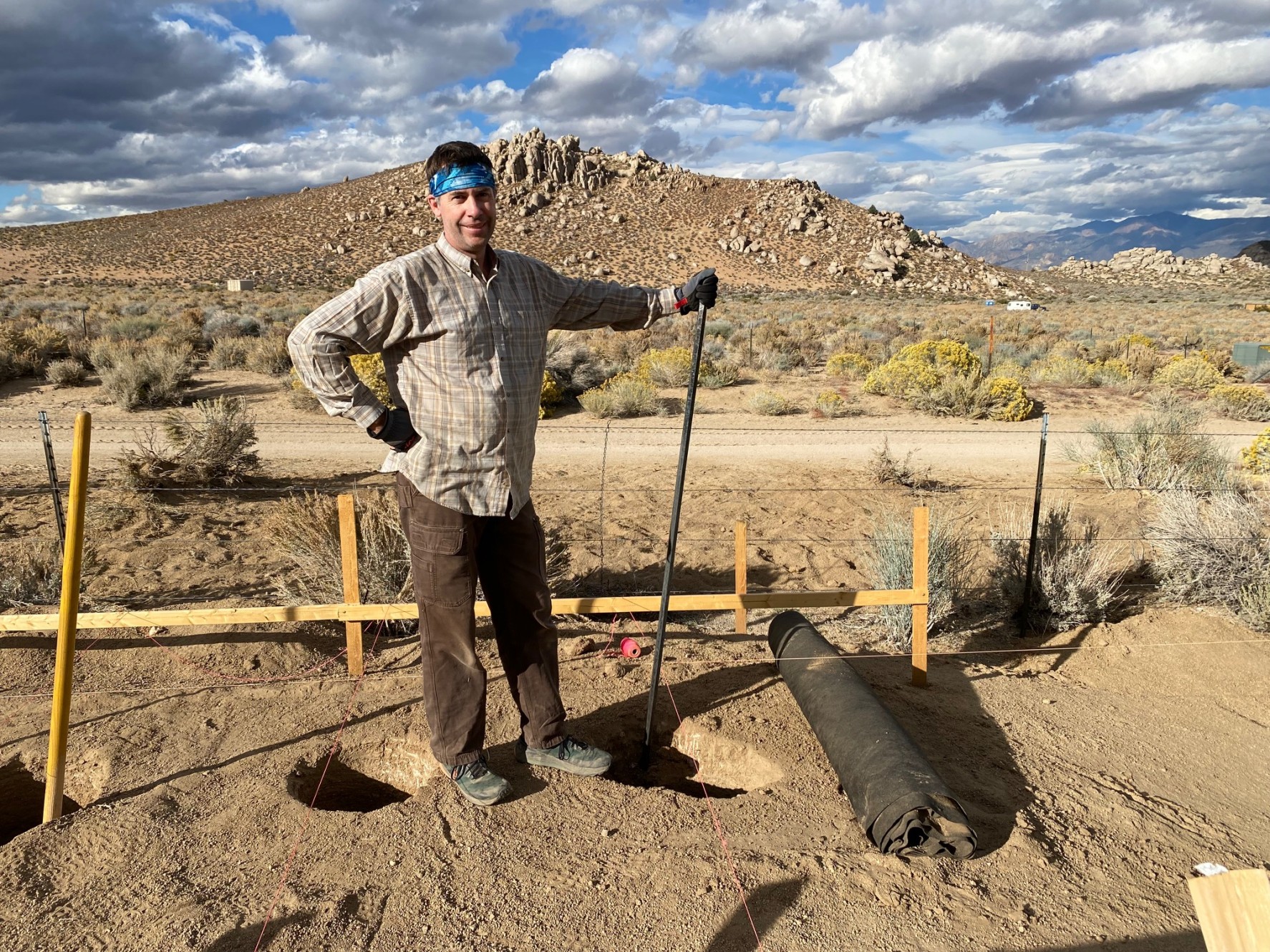 A man wears a sweat band and poses with the digging bar by a hole