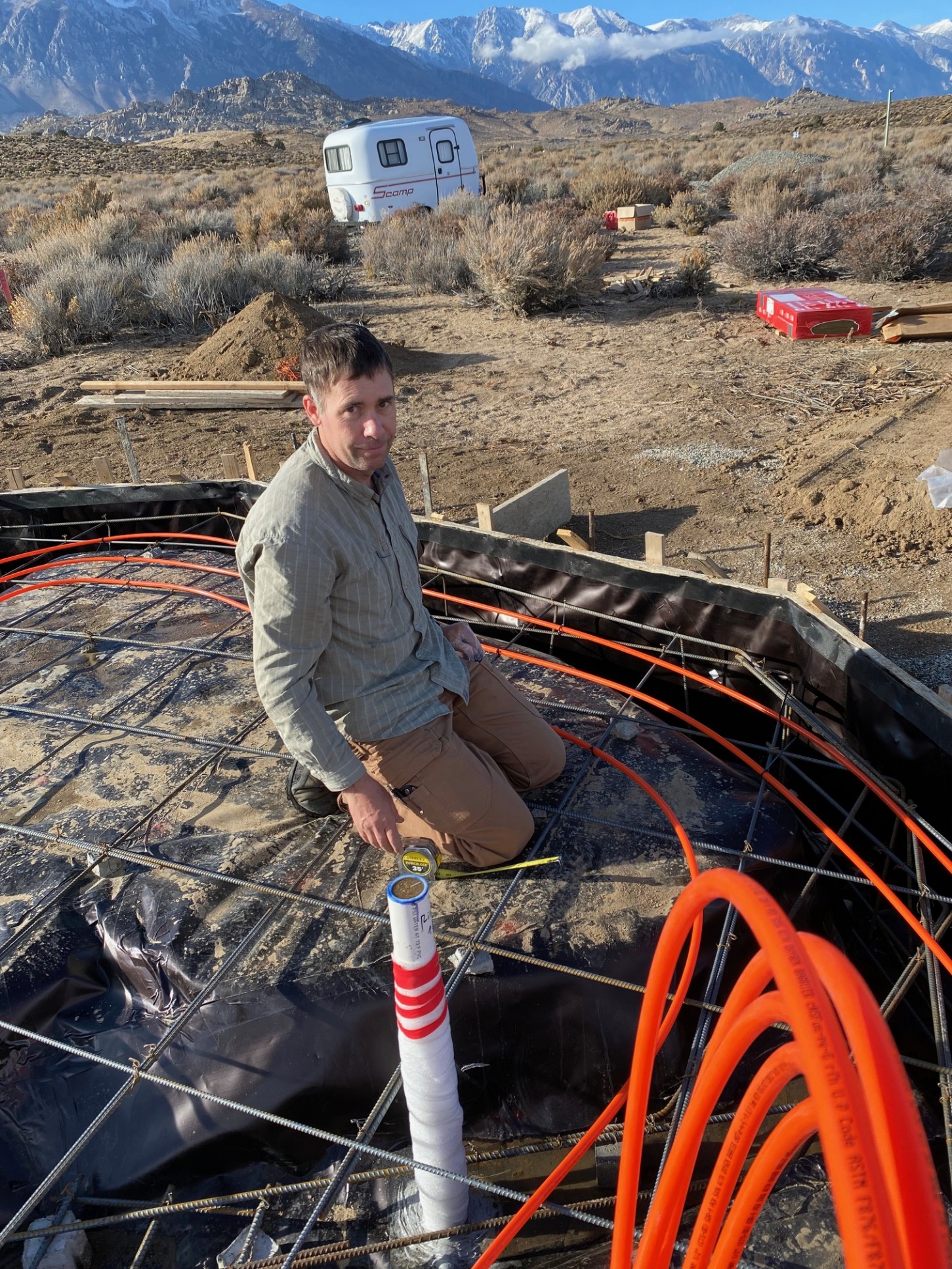 A man lays out bright orange pex on a foundation before the concrete is poured.