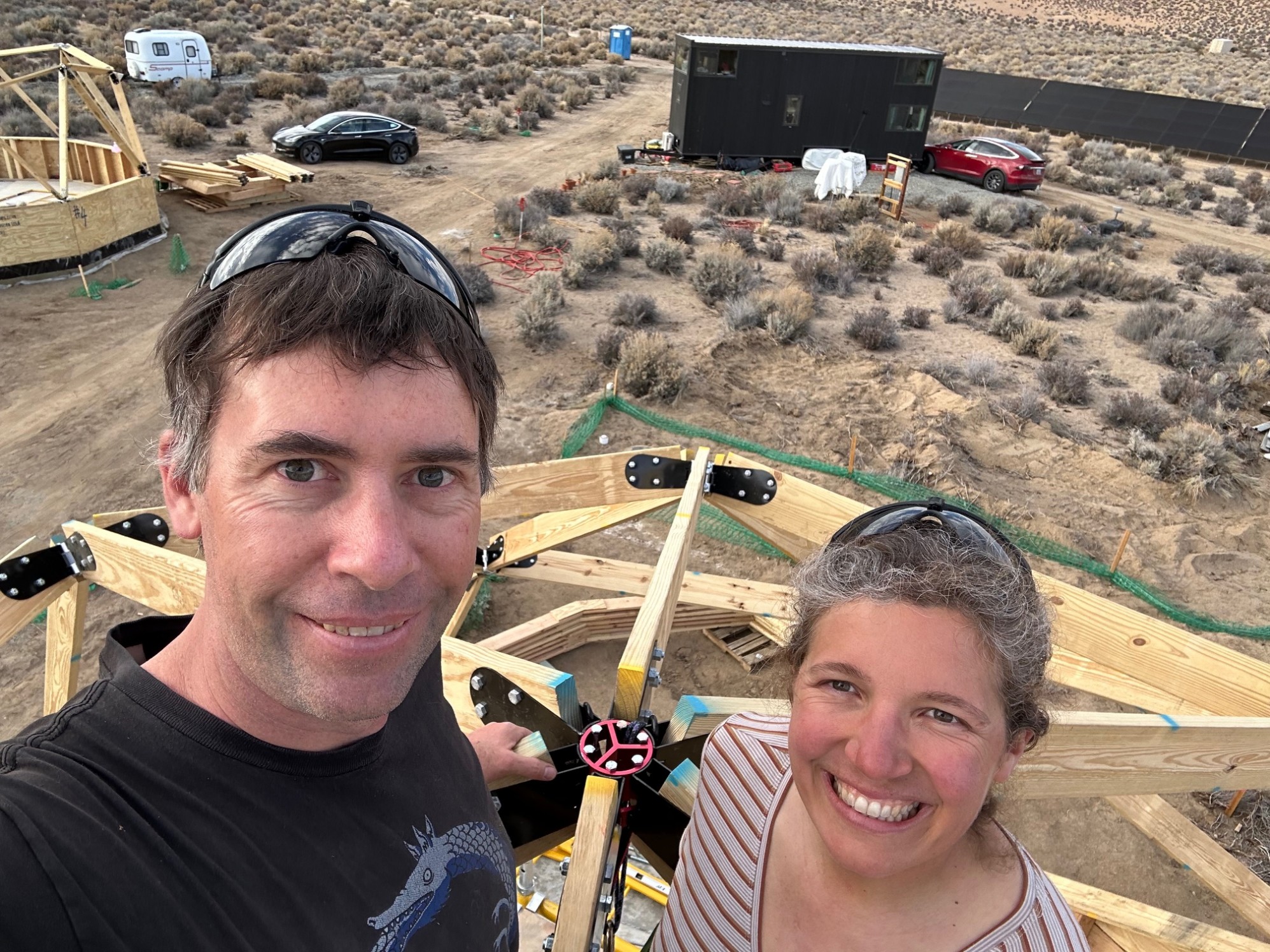 2 people smiling at the top of a partially constructed geodesic dome
