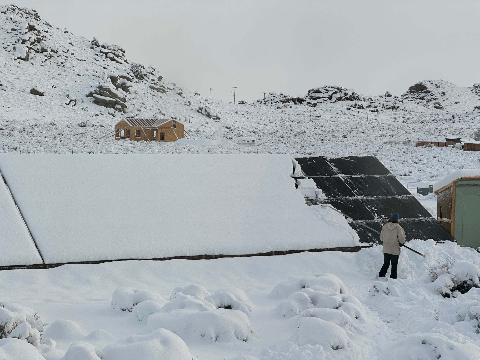 A woman uses a long snow rake to clear snow from solar panels