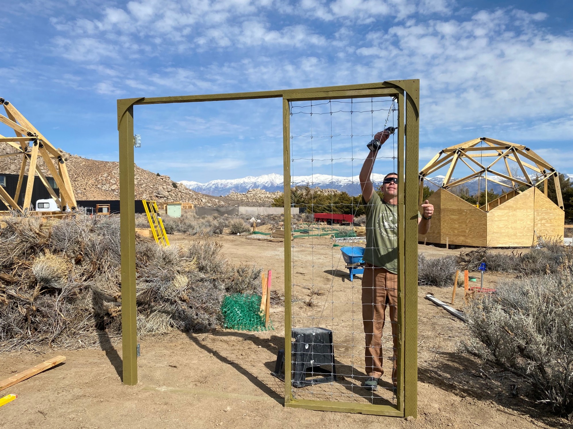 A man working on a tall green wood framed gate for a garden