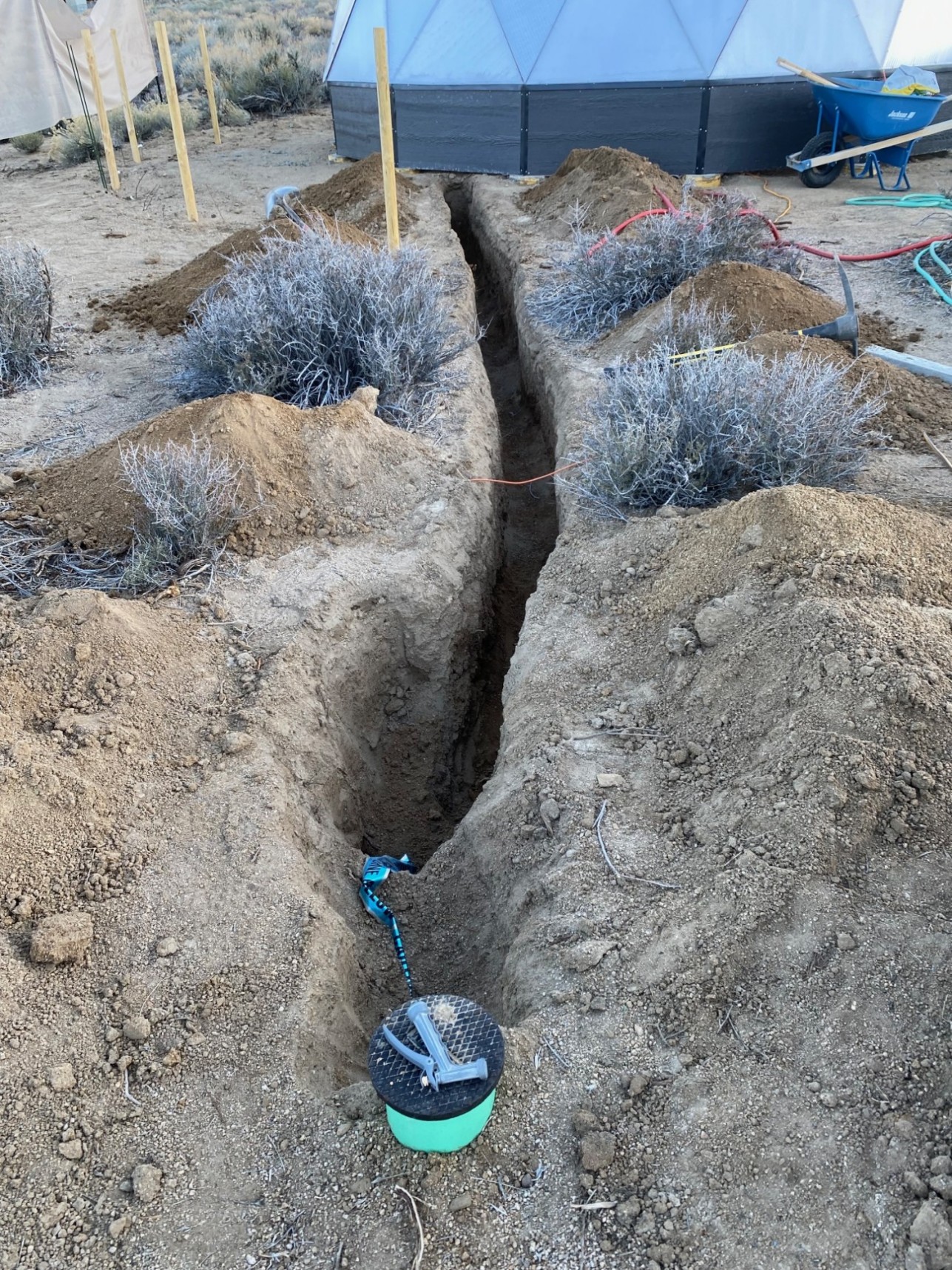 A trench snaking between a greenhouse and a water junction.