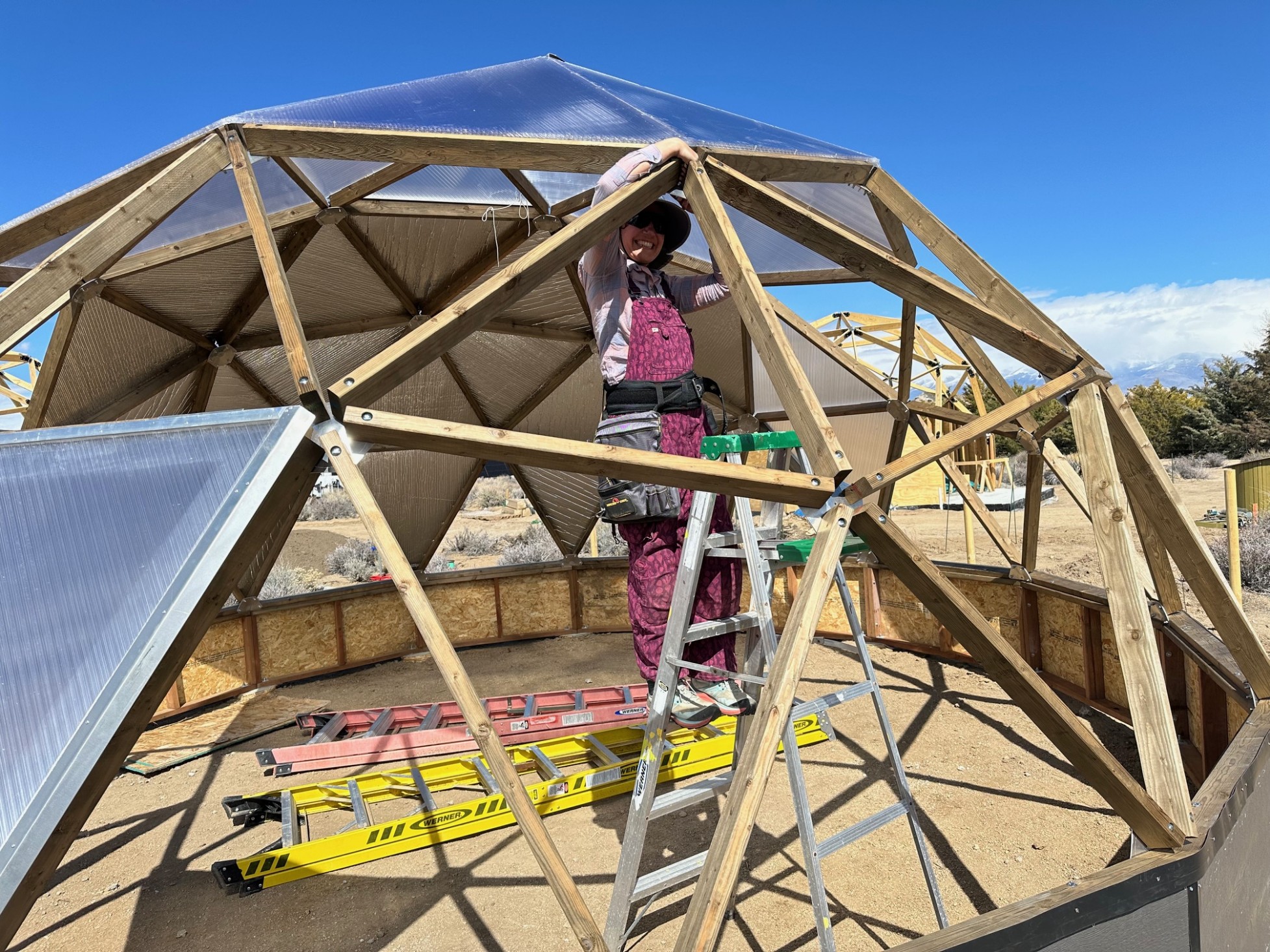 A woman on a ladder in a dome, screwing something to the frame with both hands