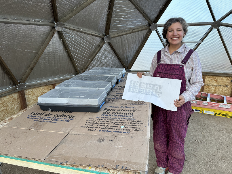 A woman holds a list next to seed starting trays inside of a dome greenhouse.