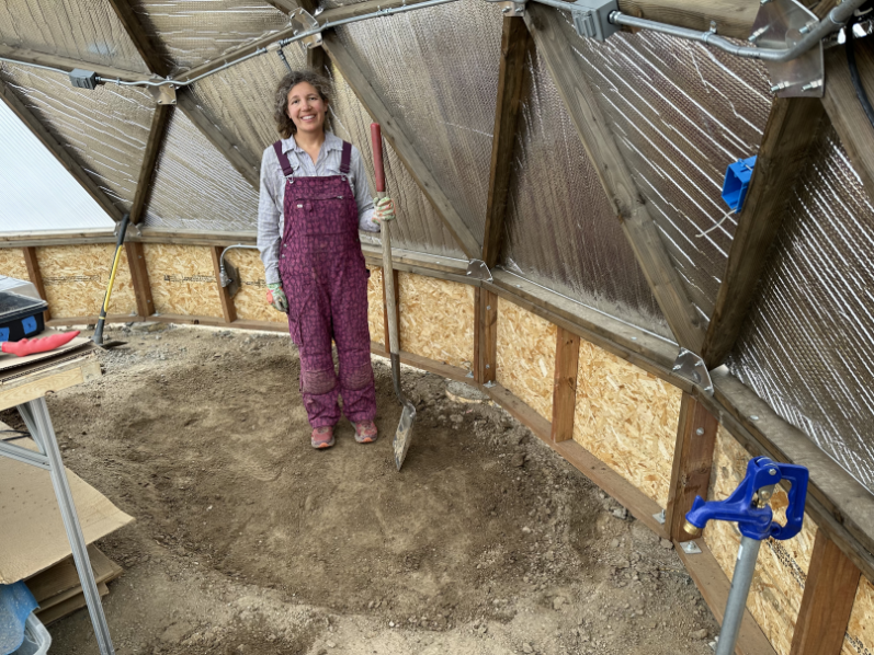 A woman posing with a shovel in a hole