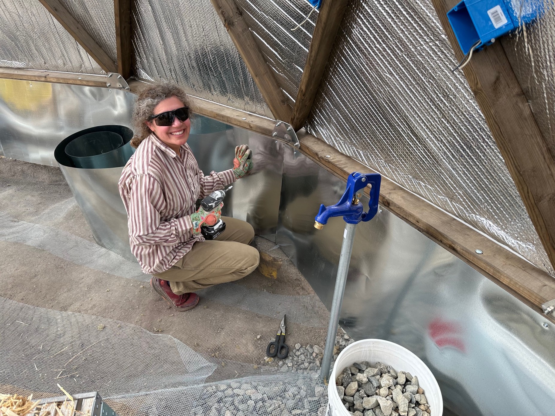 A woman drilling sheetmetal to the interior riser walls of a greenhouse dome