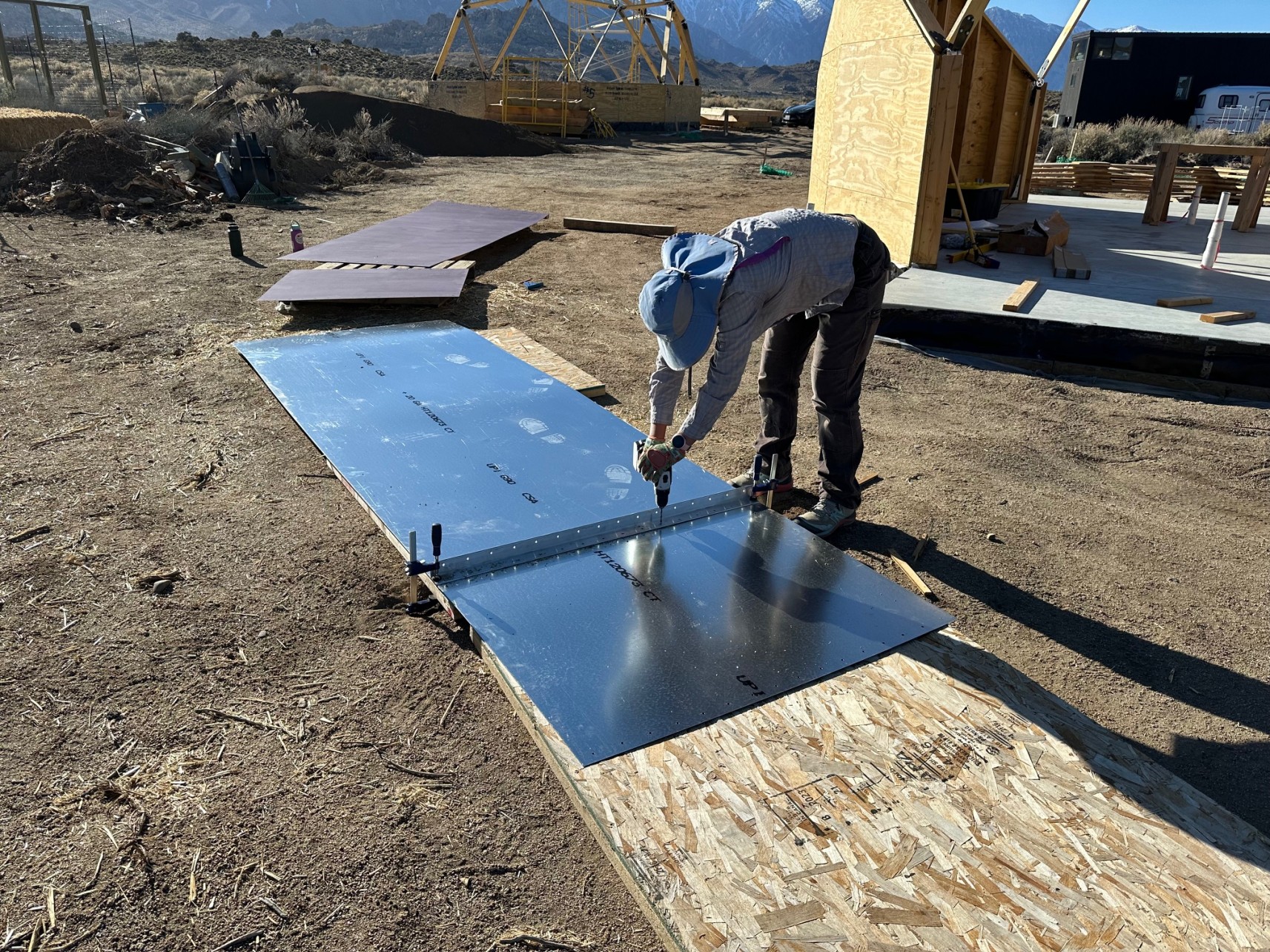 A woman bent over some sheetmetal, drilling holes into it