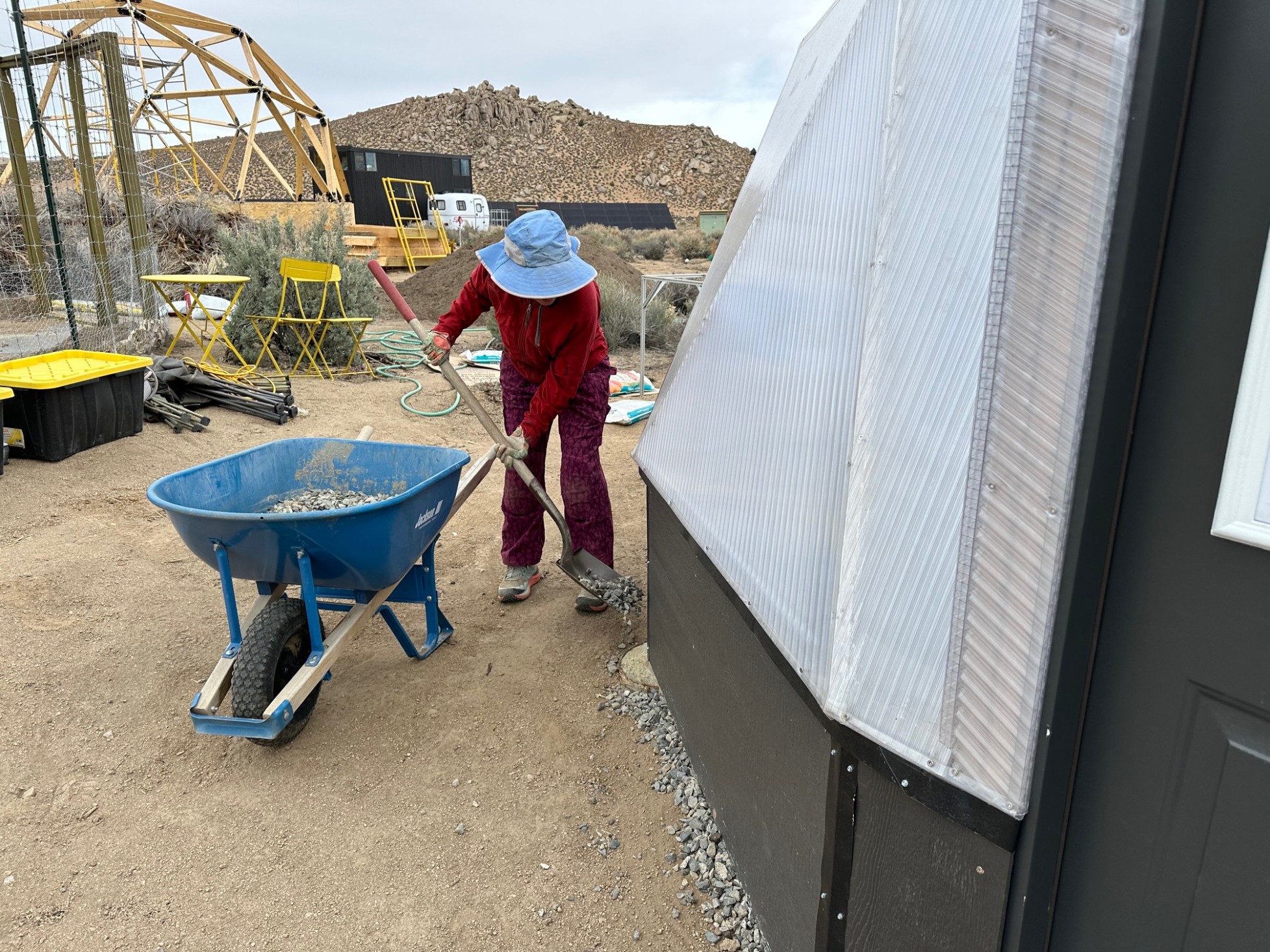 A woman shoveling gravel under the edges of a greenhouse dome