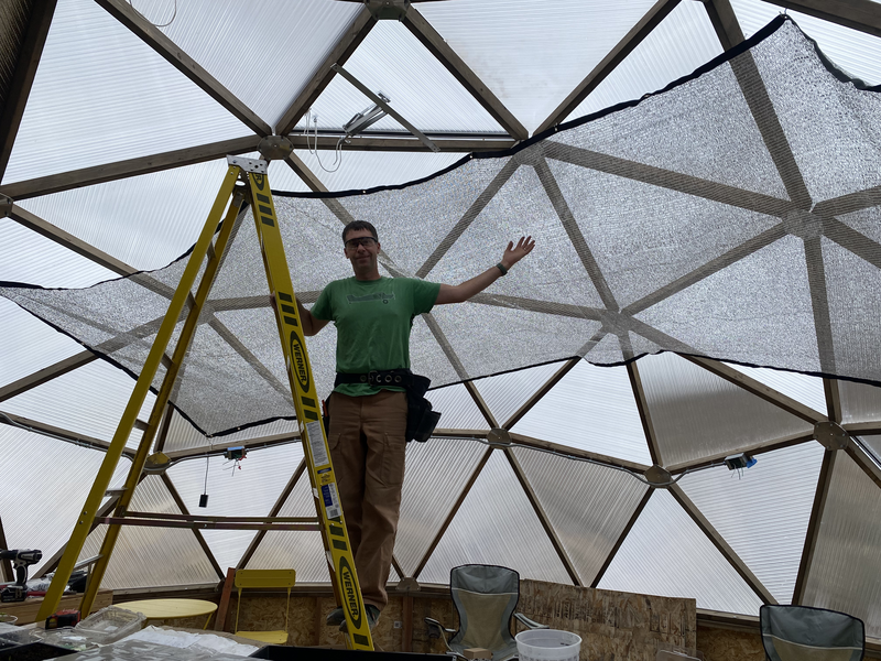 A man on a ladder posing by the shade cloth he installed