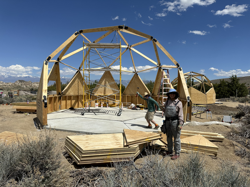 2 people pose in front of partially constructed geodesic dome