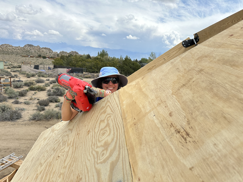 Woman peeks over the edge of plywood with nail gun