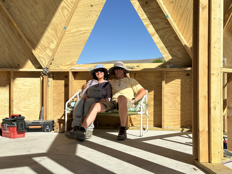 2 people relaxing on a loveseat in a partially constructed geodesic dome