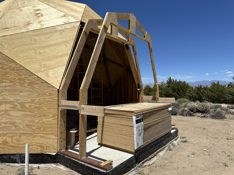 An extension with 2 of 3 arches tilted up, attached with some blocking. A large stack of plywood sits in the extension