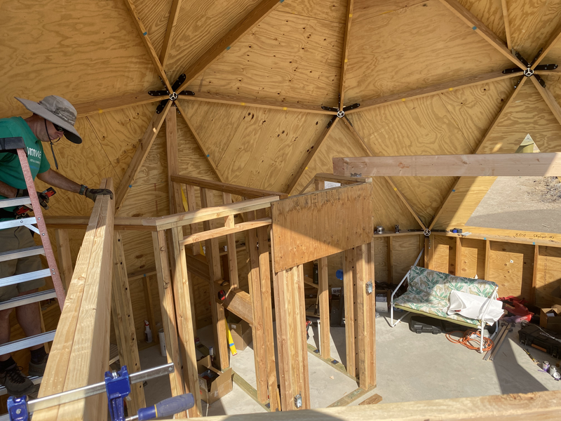 A man on a ladder above framed walls in a geodesic dome