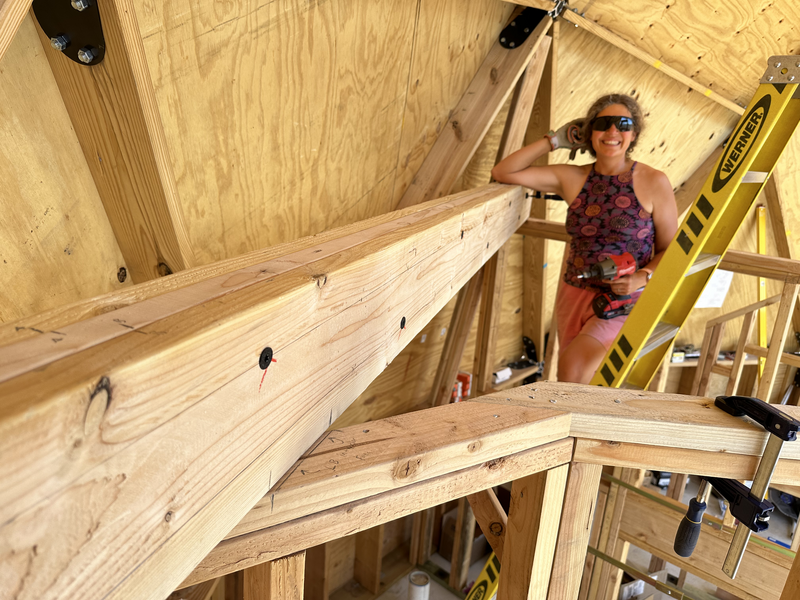 A woman leaning on a ledger board, resting a drill on her thigh